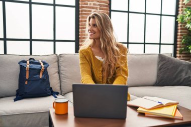 Genç, sarışın, kendine güvenen, evde dizüstü bilgisayar kullanan bir kadın.