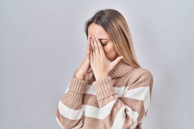 İzole edilmiş arka planda balıkçı yaka kazak giyen genç sarışın bir kadın. Ağlarken suratını ellerle kapatan üzgün bir ifade. depresyon kavramı. 