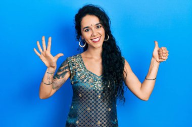 Bindi ve geleneksel kurta elbisesi giyen genç bir kadın altı numarayı gösterip işaret ederken kendinden emin ve mutlu gülümsüyor.. 
