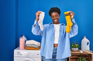 African american woman holding clean andy dirty socks smiling with a happy and cool smile on face. showing teeth. 