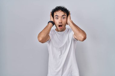 Hispanic man standing over isolated background crazy and scared with hands on head, afraid and surprised of shock with open mouth 