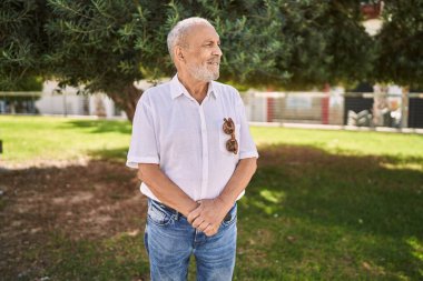 Kıdemli adam parkta kendinden emin gülümsüyor.