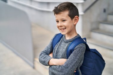 Sarışın çocuk gülümsemesi okulda kollarını kavuşturup duruyor.