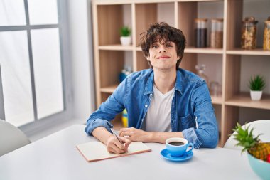 Genç İspanyol adam evde ders çalışırken deftere yazıyor.