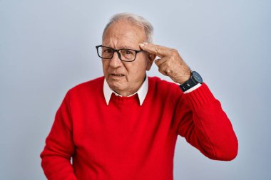 Gri saçlı yaşlı adam, izole edilmiş arka planda duruyor. Ateş ediyor ve kendini ve parmaklarını silah gibi kullanıyor. İntihar jesti.. 