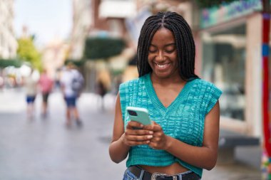 Afro-Amerikalı kadın sokakta akıllı telefon kullanarak kendine güveniyor.