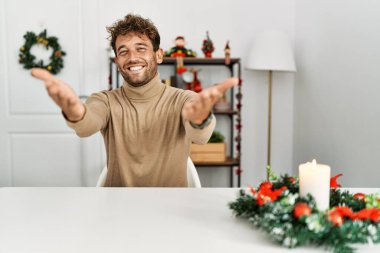 Masada sakallı genç yakışıklı adam Noel süslemelerinin yanında gülümseyen, yardım eli uzatan ve kabul gören biri.. 