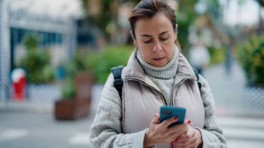 Orta yaşlı İspanyol kadın sokakta akıllı telefon kullanıyor.