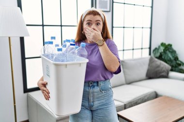 Genç kızıl saçlı kadın elinde plastik şişelerle çöp sepetini tutarken yanlışlıkla ağzı ellerle kapatıyordu. gizli kavram. 