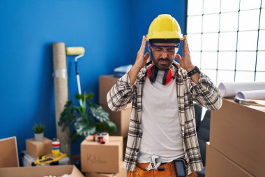 Sakallı, evde çalışan, eli başının üstünde, başı ağrıyan, genç bir İspanyol. migren ağrısı. 