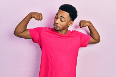 Casua tişörtü giyen genç Afro-Amerikan adam gururla gülümseyen kol kaslarını gösteriyor. fitness konsepti. 