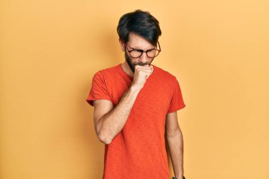 Günlük kıyafetler ve gözlük takan İspanyol genç adam kendini iyi hissetmiyor ve soğuk algınlığı veya bronşitin belirtisi olarak öksürüyor. sağlık hizmeti kavramı. 
