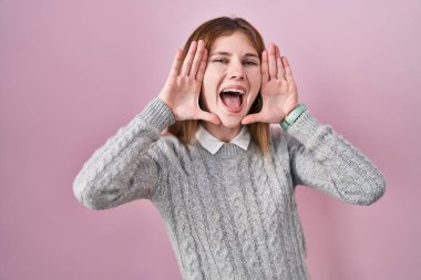 Beautiful woman standing over pink background smiling cheerful playing peek a boo with hands showing face. surprised and exited 