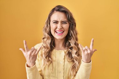 Sarı arka planda duran beyaz bir kadın çılgın bir ifadeyle el kaldırarak rock sembolü yapıyor. Müzik yıldızı. ağır kavram. 