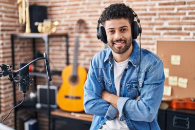 Genç Arap müzisyen, müzik stüdyosunda kollarını kavuşturup gülümsüyor.