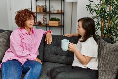 Olgun anne ve Down sendromlu kız evde, kanepede oturmuş sohbet ediyorlar.