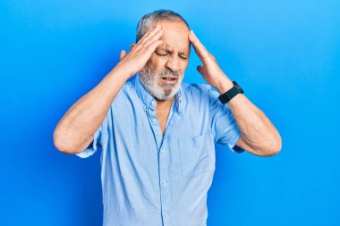 Sakallı, sıradan mavi tişörtlü, baş ağrısı çeken, çaresiz ve stresli yakışıklı bir adam. Çünkü acı ve migren ağrısı var. Eller başının üstünde.. 