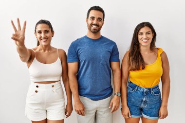 İzole edilmiş arka planda duran bir grup İspanyol genç üç numaralı parmaklarını gösterip işaret ederken kendinden emin ve mutlu gülümsüyor.. 