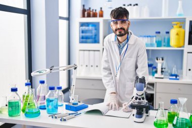 Young hispanic man scientist writing on notebook working at laboratory