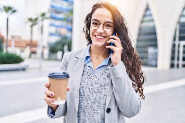 Genç İspanyol kadın yönetici kahve içiyor ve caddede akıllı telefondan konuşuyor.