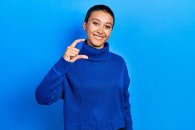 Kısa saçlı, balıkçı yaka kazak giyen, gülümseyen, kendine güvenen, el hareketi yapan, parmaklarıyla işaret yapan ve kameraya bakan güzel İspanyol bir kadın. ölçüm kavramı. 