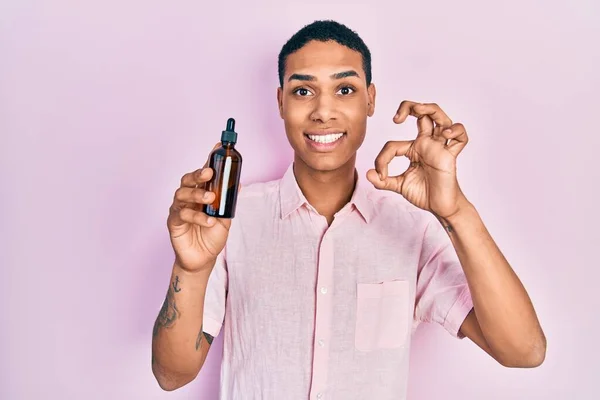 Young African American Guy Holding Serum Bottle Doing Sign Fingers — Stockfoto