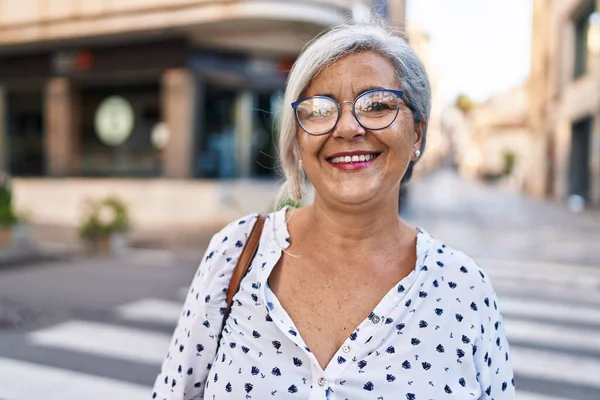 Orta yaşlı bir kadın sokakta kendine güvenerek gülümsüyor.