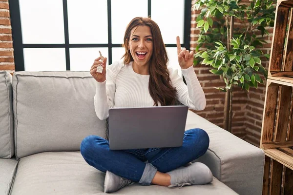 Young Brunette Woman Using Laptop Holding Keys New Home Surprised — Stockfoto