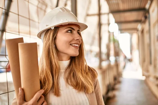 Young blonde woman wearing hardhat holding blueprints at street