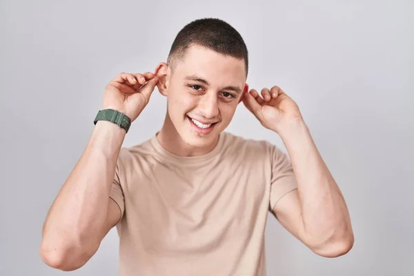 Junger Mann Vor Isoliertem Hintergrund Lächelnd Mit Fingern Ohren Zuziehend — Stockfoto