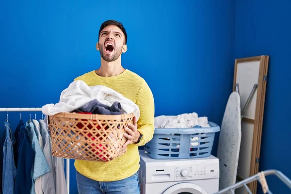 Hispanic Man Holding Laundry Basket Angry Mad Screaming Frustrated Furious — Stockfoto