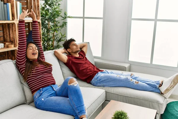 Genç Latin çift esnemekten ve kollarını esnetmekten yoruldu. Evdeki kanepede oturuyorlar..