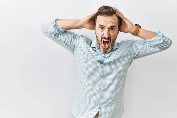 Middle age hispanic man with beard standing over isolated background crazy and scared with hands on head, afraid and surprised of shock with open mouth