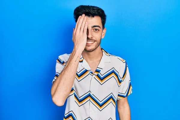若いヒスパニック系の男は手で一つの目をカバーカジュアル服を着て 顔に自信を持って笑顔と驚きの感情 — ストック写真