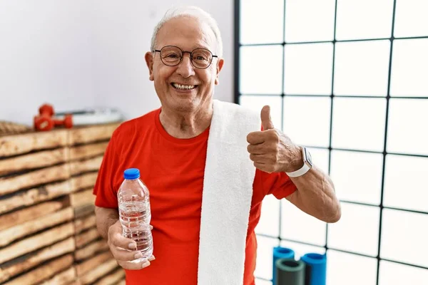 Senior man wearing sportswear and towel at the gym doing happy thumbs up gesture with hand. approving expression looking at the camera showing success.