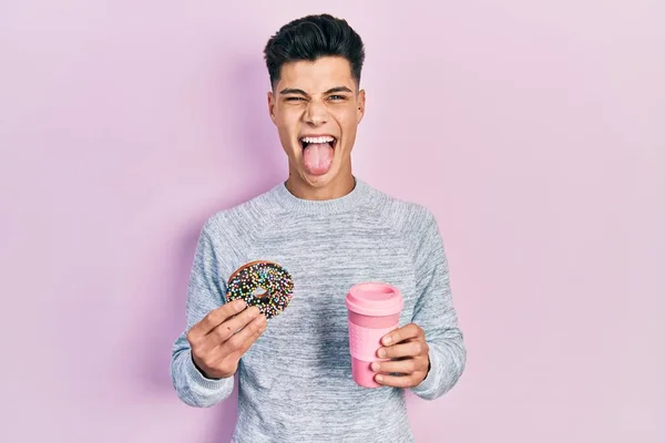 Jovem Hispânico Homem Comer Donut Beber Café Furar Língua Feliz — Fotografia de Stock