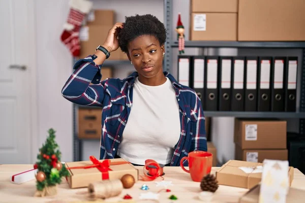 African american woman working at small business doing christmas decoration confuse and wonder about question. uncertain with doubt, thinking with hand on head. pensive concept.