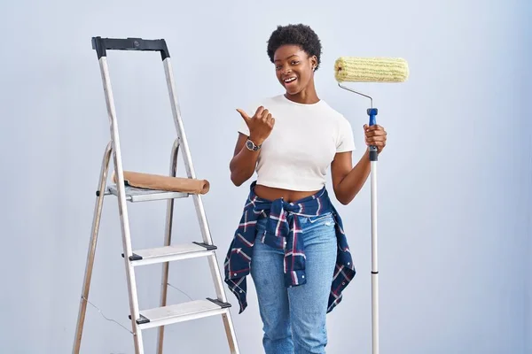 African American Woman Holding Roller Painter Pointing Back Hand Thumbs — Foto Stock