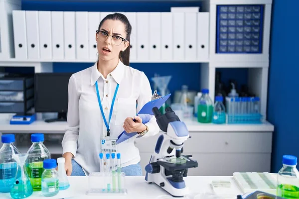 Young Brunette Woman Working Scientist Laboratory Shock Face Looking Skeptical — Stockfoto