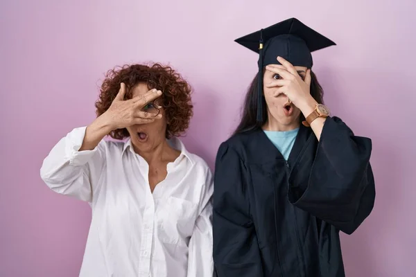 Hispanic Mother Daughter Wearing Graduation Cap Ceremony Robe Peeking Shock — ストック写真