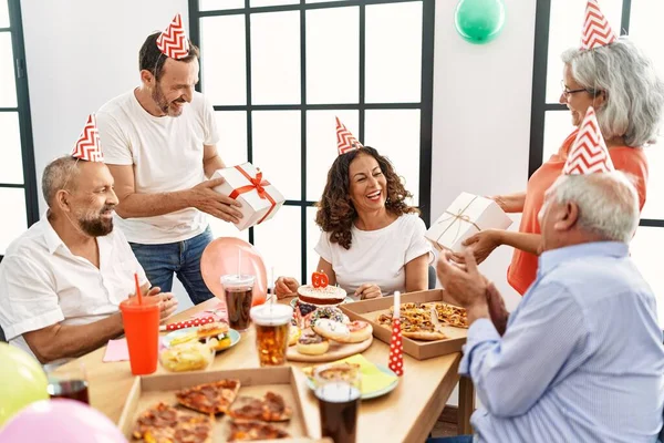 Group of middle age friends celebrate birthday giving gifts at home
