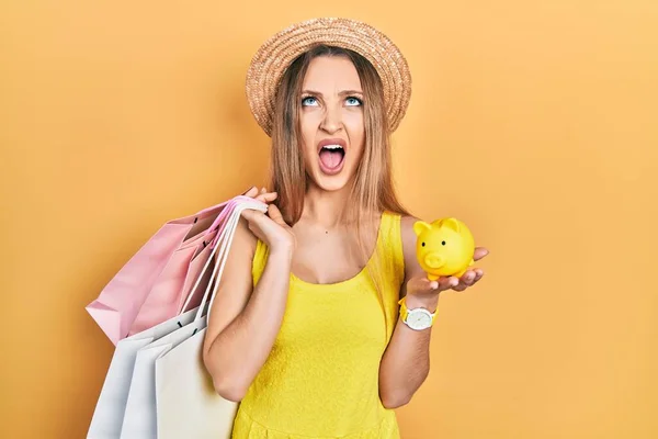 Young Blonde Girl Holding Shopping Bags Piggy Bank Angry Mad — Stock Photo, Image