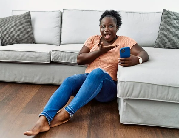 Young African Woman Using Smartphone Sitting Floor Home Pointing Aside — 图库照片