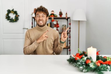Yılbaşı süslemeleriyle masada oturan sakallı genç ve yakışıklı bir adam iki eli de endişeli ve şaşırmış bir ifade takınıyor. 