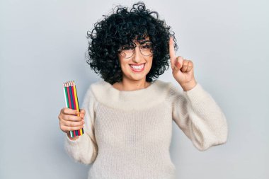 Orta Doğulu genç bir kadın elinde renkli kalemlerle gülümseyen bir fikir ya da soruyla mutlu bir yüzü işaret eden bir numara. 