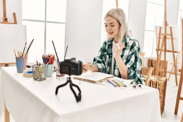 Young artist student girl dmiling happy painting. Sitting on desk recording art class at art studio.