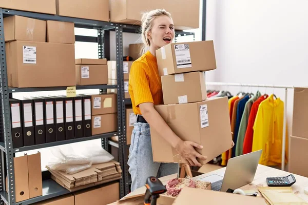 Young blonde woman working at small business ecommerce winking looking at the camera with sexy expression, cheerful and happy face.