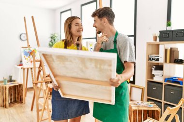 Genç İspanyol sanatçı çift resim stüdyosunda tuval tutarken mutlu gülümsüyor..