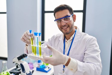 Young hispanic man scientist holding test tubes at laboratory