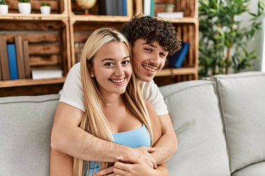 Kanepede oturan genç çift evde sarılıyorlar..